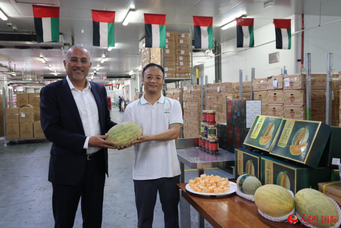 在位于迪拜的物流冷库，阿联酋中国新疆商会会长阿不来提（左）与新疆果业代表共同展示此次运抵的蜜瓜产品，人民网记者张志文摄